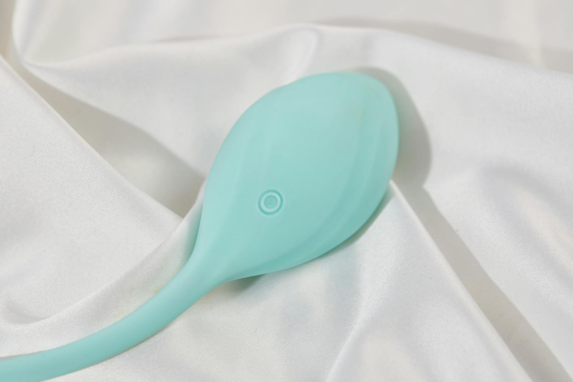A stylish teal clitoral vibrator on white silk fabric, representing pleasure tools for different cycle phases