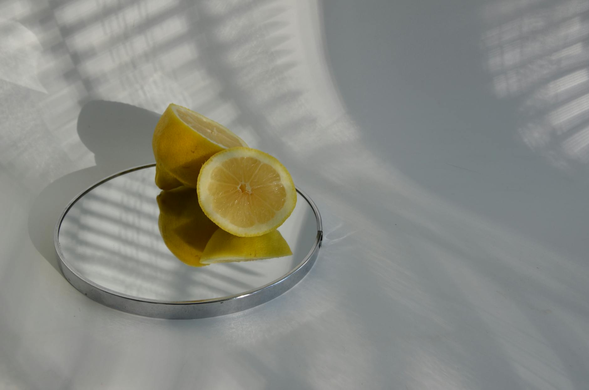 Sliced lemons on a mirror casting shadows, showcasing minimalistic food photography