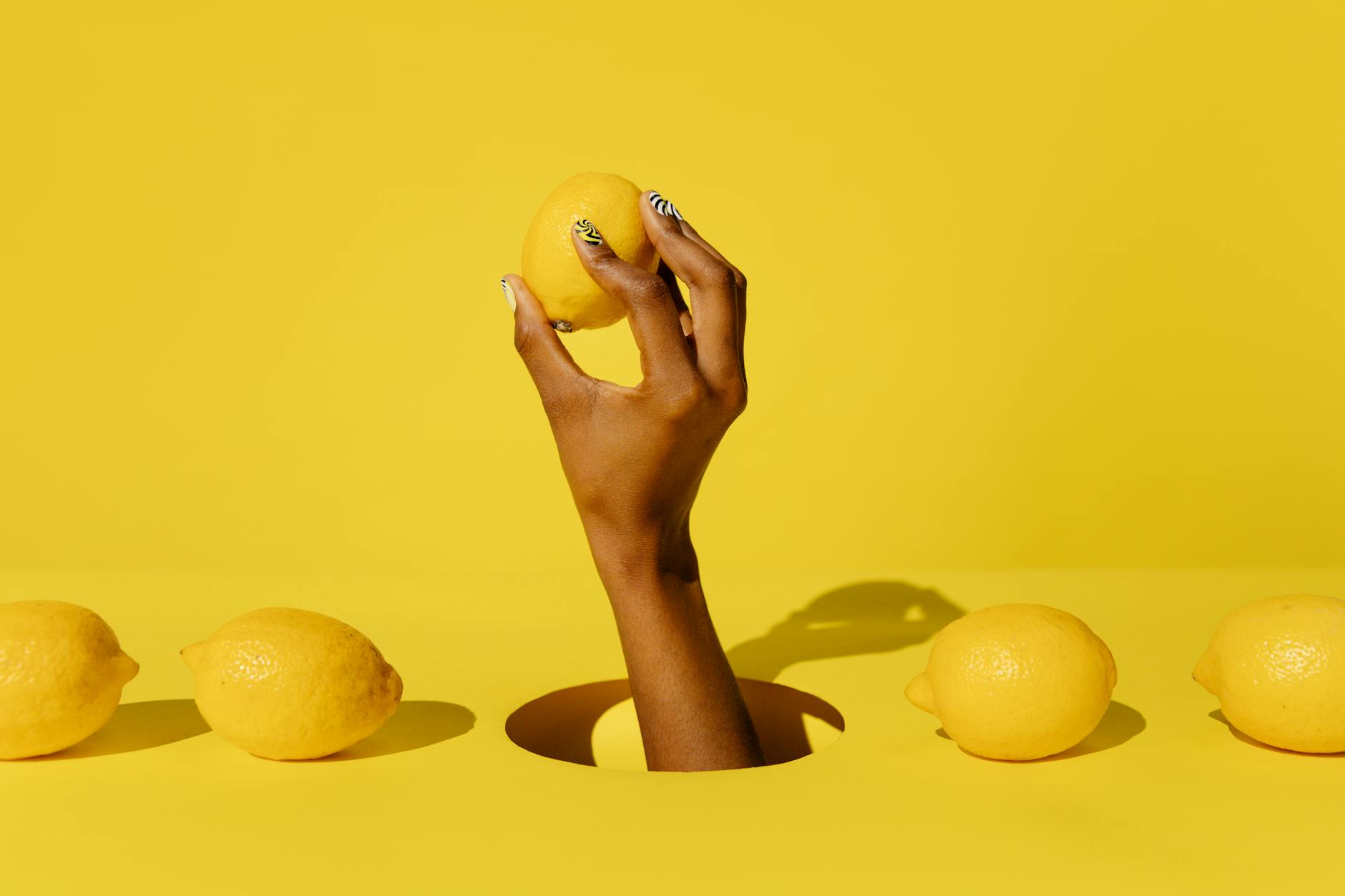 A hand holding a fresh lemon against a vibrant yellow background, representing renewal and fresh sensation