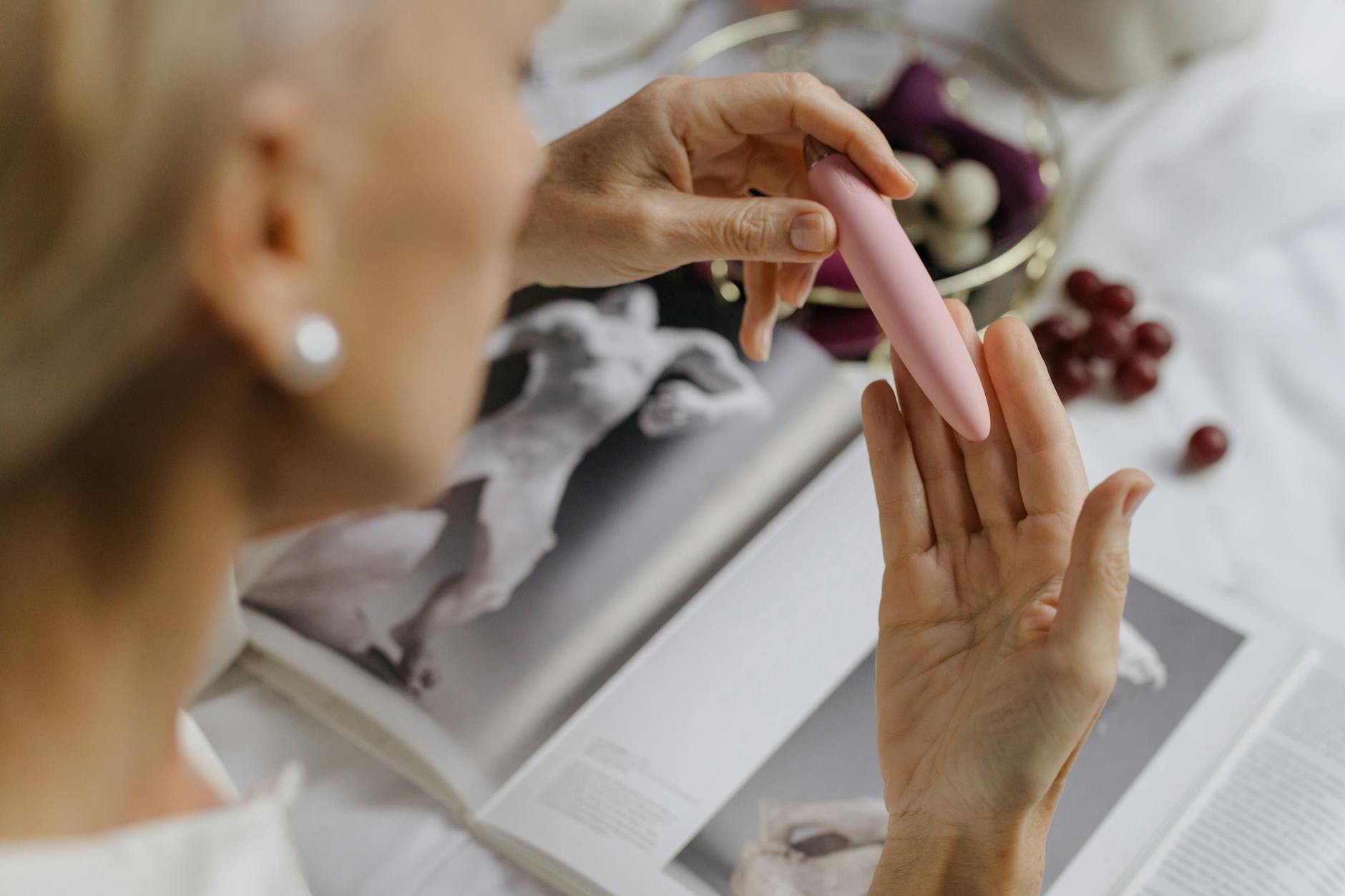 Close-up of a hand holding a pink vibrator with art books in soft focus background, symbolizing intimate exploration