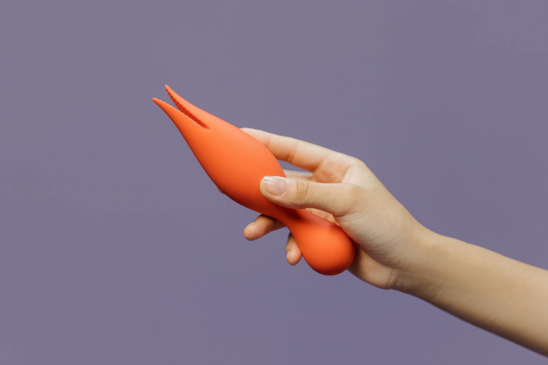 A hand holding a vibrator against a minimalistic purple backdrop