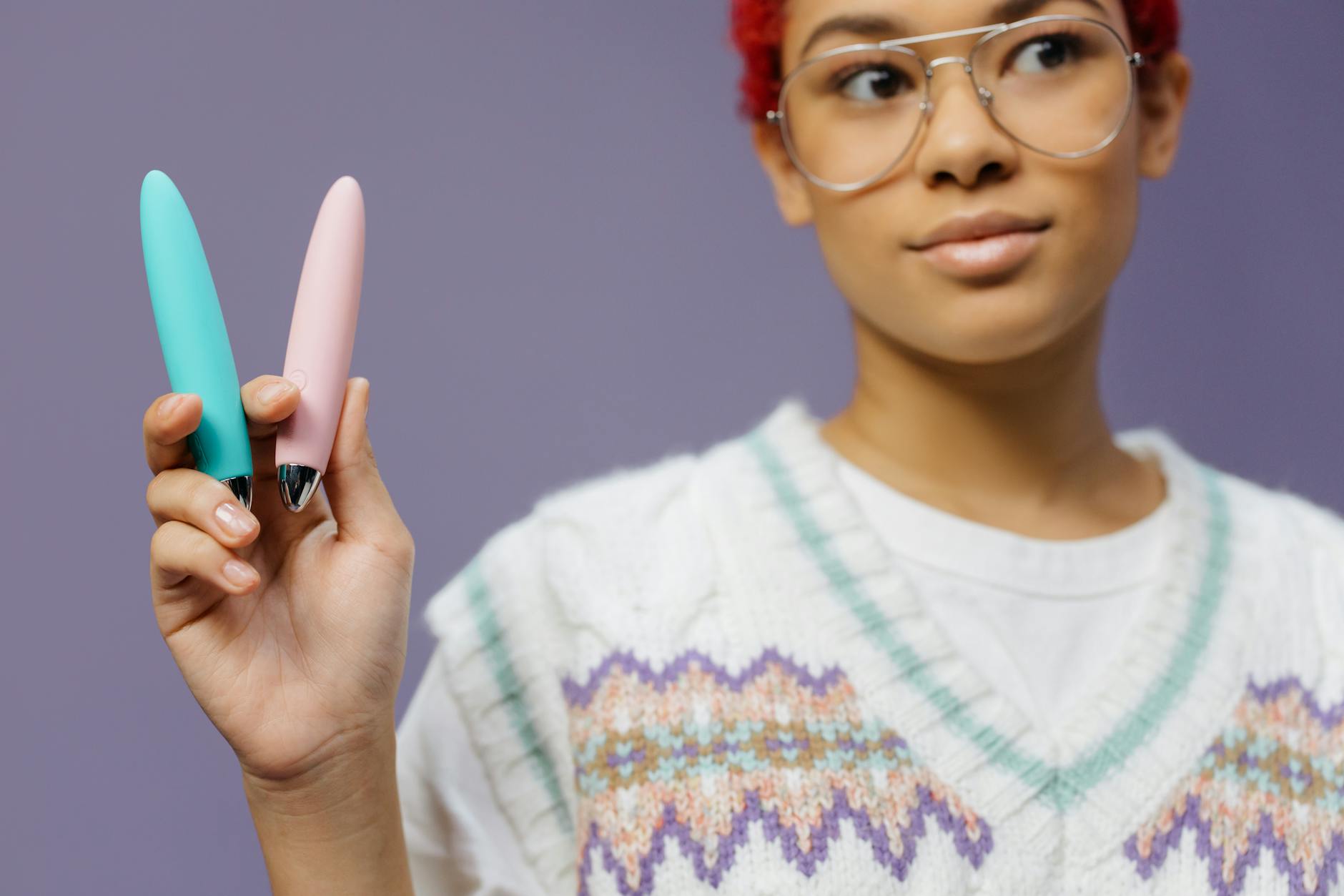 A woman holding two colorful vibrators against a purple background, symbolizing self-exploration