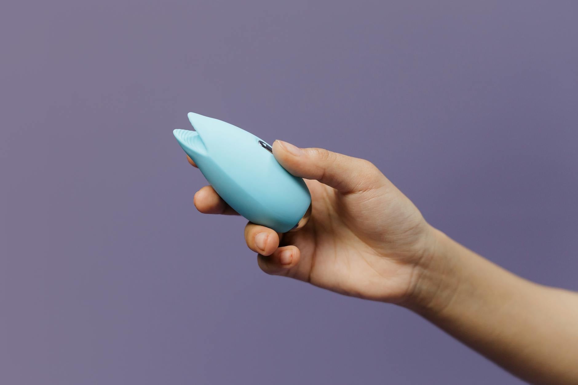 A hand holding a blue silicone vibrator against a purple background, representing self-care and intimate wellness