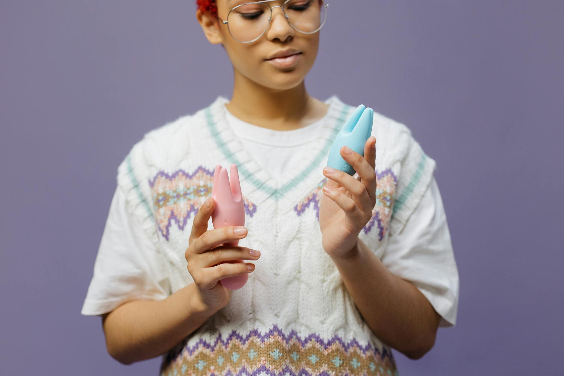 Woman holding blue and pink silicone clitoral vibrators, considering comfort options for sensitive areas.